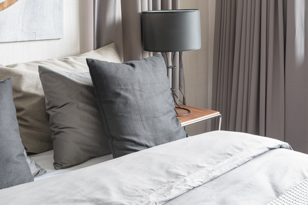 grey pillow on white bed in modern bedroom with black lamp on wooden tableの写真素材