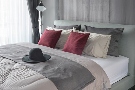 red pillows and black hat on bed in modern bedroom designの写真素材
