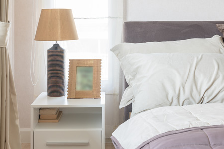 white pillow on bed with picture frame and lamp on table sideの写真素材