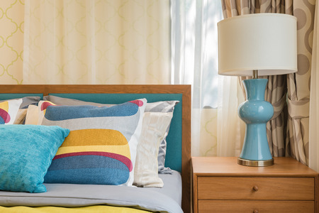 colorful pillows on wooden bed in modern bedroom design with white lampの写真素材