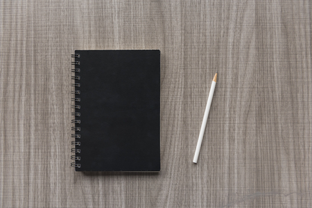 white pencil and black notebook on wooden tableの写真素材