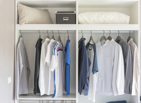 clothes hanging in white closet with white pillows and boxの写真素材