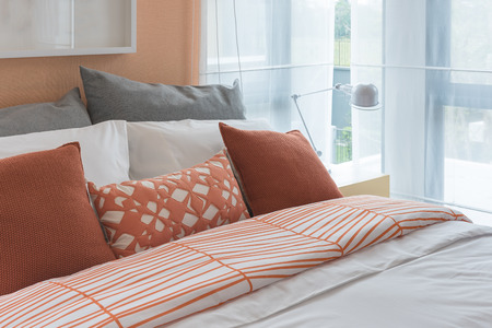orange color tone pillows set on bed in modern bedroom designの写真素材