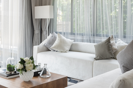 luxury white sofa with pillows set in living room with vase of flower on wooden tableの写真素材