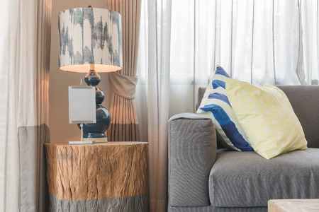 set of pillows on modern grey sofa in living room with lamp on wooden table sideの写真素材