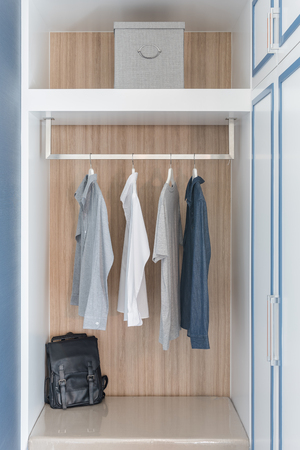 clothes hang on rail in wooden closet with black bagの写真素材