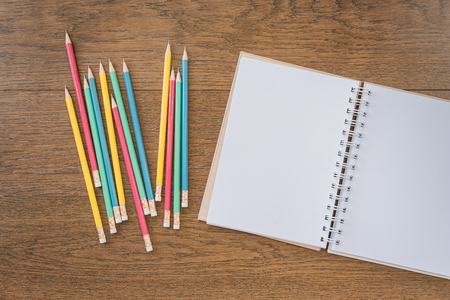 multicolor pencils and blank notebook on wooden background with copy spaceの写真素材