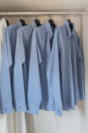 row of blue color shirts hanging on rail in wooden wardrobeの写真素材