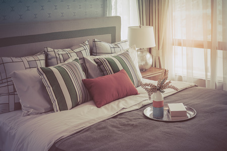 colorful pillows on white bed in modern bedroom design with tray of book and plant, vintage process styleの写真素材