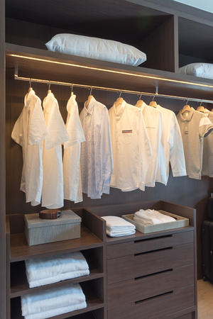 row of white shirts on rail in wooden closet, interior design conceptの写真素材