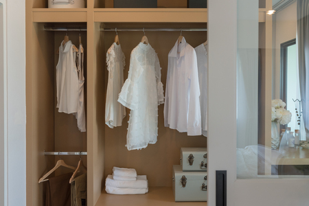 modern closet with clothes hanging on rail, white wooden wardrobe, interior design conceptの写真素材