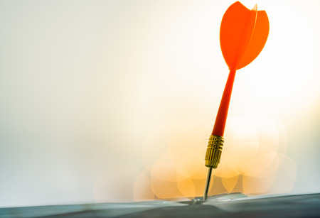 Red dart arrow hitting in the target center of dartboard with city background. Target business, achieve and victory concept.の写真素材