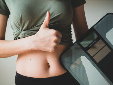 Slim sporty Woman holds weight scale and shows like or thumb up. People, sport, fitness and health concept. Selective focus.の写真素材