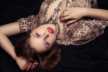 Glamor portrait of beautiful woman lying on black bedの写真素材