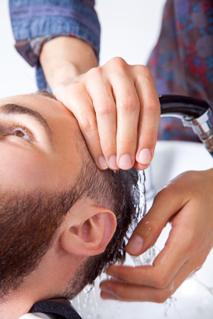 Hairstyling. Cropped image of barber washing head of his client in barber shop while preparing to haircutの写真素材