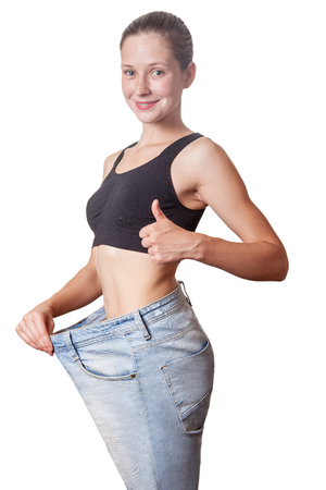Close-up of slim waist of young woman in big jeans showing successful weight loss, isolated on white background, diet concept.の写真素材