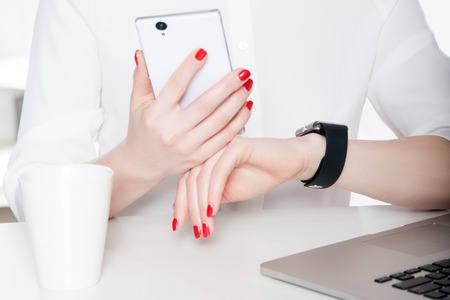 Top view of woman hand with smartwatch. with keyboard of laptop and smartphone on background....
