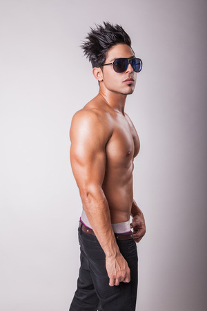 Shirtless attractive middle eastern fashion model muscular guy in black jeans standing on podium on grey background.の写真素材