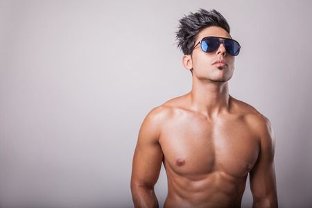 Shirtless attractive middle eastern fashion model muscular guy in black jeans standing on podium on grey background.の写真素材