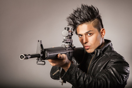 Young middle eastern man with black leather jacket in black suit holding gun. studio shot.の写真素材