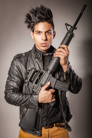 Young middle eastern man with black leather jacket in black suit holding gun. studio shot.の写真素材