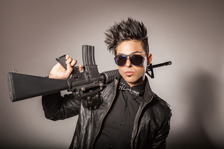 Young middle eastern man with black leather jacket in black suit holding gun. studio shot.の写真素材