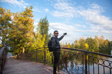 Portrait of the young bearded handsome fashion traveler in the park with casual style and fashion...