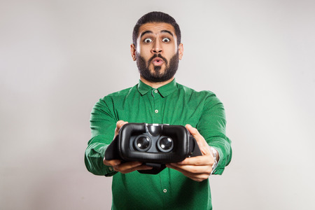 Young emotional middle eastern excited man with beard and green shirt using a VR headset and experiencing virtual reality.の写真素材