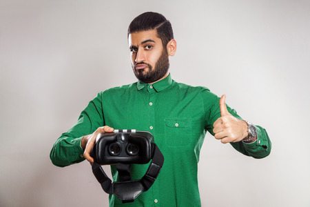 Young emotional middle eastern excited man with beard and green shirt using a VR headset and experiencing virtual reality.の写真素材