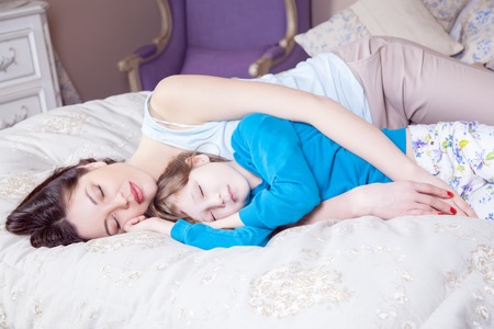 Careful young mother putting down her little daughter. Happy family. Studio shot.