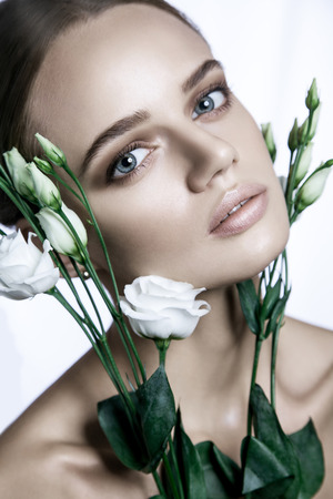 Calm Beauty Fashion Model Woman face. Portrait with white Rose flower. Beautiful Blonde Woman with blue eyes and Nude Makeup. studio shot.の写真素材