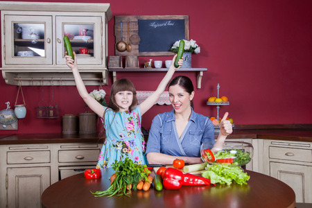 Happy mother and daughter enjoy making and having healthy meal together at their kitchen. they are making vegetable salad and having fun together. mom take care of her daughter and tech how to cook.の写真素材