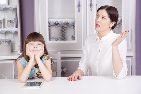 Mother and daughter quarrel because of overuse the tablet phone (computer, tablet, etc.). Social problem between parents and children. Studio shot.の写真素材