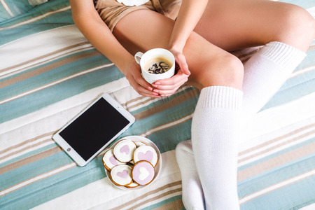 Woman using tablet at cozy home atmosphere on the bed. Young woman with cup of cocoa or coffee in hands enjoying free time with comfort. Soft light and comfy lifestyle concept. top view point.の写真素材