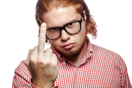 Angry bearded readhead businessman with red shirt and freckles looking at camera and showing middle finger (fuck). studio shot isolated on white.の写真素材