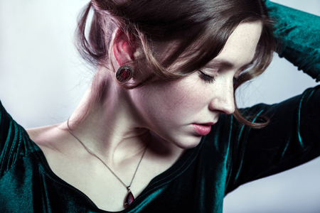 Portrait of beautiful woman with makeup, hairstyle and natural freckles on her face in green dress posing with closed eyes on silver gray background.の写真素材