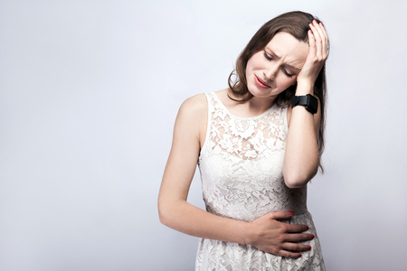 Portrait of beautiful woman with freckles and white dress and smart watch with stomach pain on silver gray background. healthcare and medicine concept.の写真素材