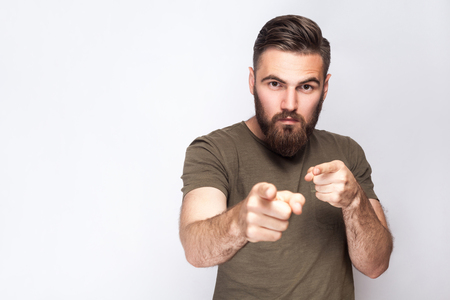 Hey You! Portrait of serious bearded man with dark green t shirt against light gray background. studio shot.の写真素材