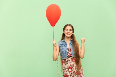 Its winn! The beautiful blonde teenager with red balloons on a green background. Isolated studio shotの写真素材