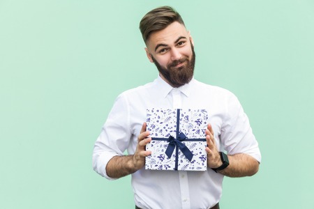 Gift with love. Interesting bearded young adult man with a gift box on light green background. Studio shotの写真素材