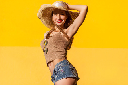 Elegance young adult model in casual top, jeans short and hat. Studio shot on yellow background, outdoorの写真素材
