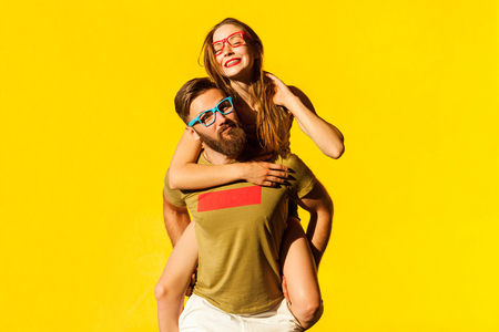 Piggyback. Happiness friend looking at camera and posing on yellow background. Studio shotの写真素材