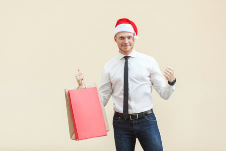 Buy for best price in winter. Young adult and beard man in red santa hat ,happiness looking at camera. Indoor, studio shot on light orange backgroundの写真素材