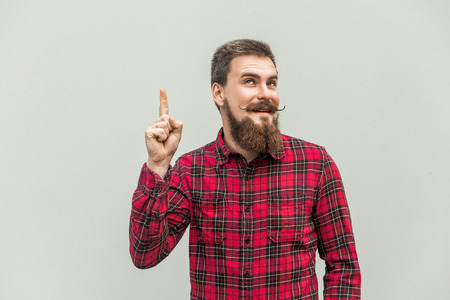 I have idea! Handsome businessman with beard and handlebar mustache looking at camera with finger up. studio shot, on gray background.の写真素材