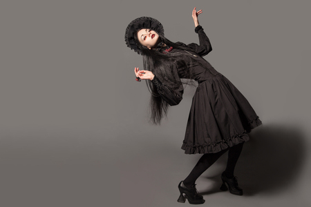 Portrait of brunette woman in black dress and classic gothic style with red eyes on gray background. halloween concept.の写真素材