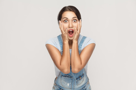 Human face expressions and emotions. Arab young adult woman holding arms on her cheeks and shocked. Isolated on gray background, studio shotの写真素材