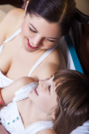 Closeup. Portrait of mother and young girl lie in bed in the morning, hugging , smiling and looking at each other. Studio shotの写真素材