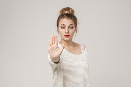 Blone young adult woman showing stop or ban sign. Studio shot, gray backgroundの写真素材