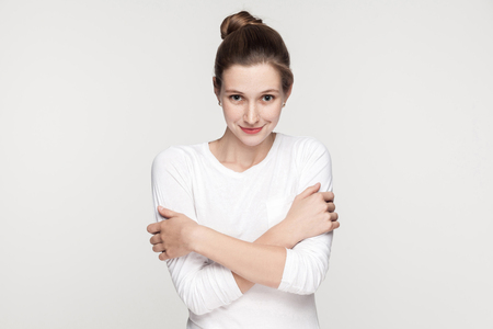 Attractive beautiful freckles woman embrace himself and looking at camera. Studio shot, isolated on gray backgroundの写真素材