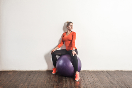 Sexy blonde woman sit on fitness bal near light gray wall. Indoor shotの写真素材